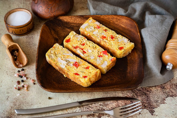 Pieces of chicken roll with pepper on a wooden platter on a gray background