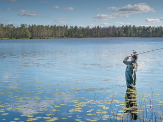 Obraz premium Karelia, Vodlozero - 29.07.2019: Young man fishing with spinning in lake. Ecotourism, visiting fragile, pristine, undisturbed natural areas. Active holidays in Karelia. Portrait