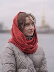 Portrait of a girl in a down jacket and a red scarf on the background of the Neva River