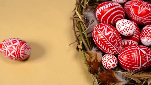Easter red eggs with folk white pattern into bird nest on paper background. Man's hand add eggs to nest. Ukrainian traditional eggs pisanka and krashanka.