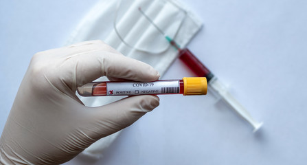 close-up of a positive covid-19 blood test on hand with surgical mask and syringe background.