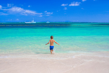A 5 year old boy enters the calm and beautiful sea alone. European child on the background of the Caribbean Sea, from the back.