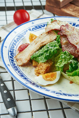 Caesar salad with croutons, parmesan, chicken, egg in a white stylish bowl. Restaurant serving. Selective focus, wooden background