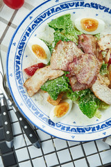 Caesar salad with croutons, parmesan, chicken, egg in a white stylish bowl. Restaurant serving. Selective focus, wooden background