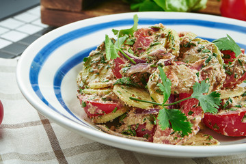 Georgian vegetable salad with tomatoes, cucumber and onions seasoned with walnut sauce in a white bowl. Salad in a composition with ingredients. Close up.