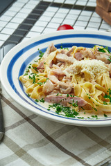 Italian fettuccine pasta in cheese sauce with parmesan, chicken and ham, herbs in white ceramic bowl on white background.