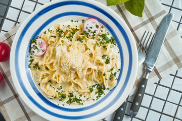 Italian fettuccine pasta in cheese sauce with parmesan, cherry tomatoes and herbs in white ceramic bowl on white background. Tasty food background