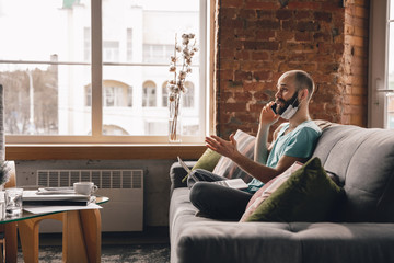 Obraz premium Talking on phone. Young man doing yoga at home while being quarantine and freelance online working. Remote office, isolated. Concept of healthy lifestyle, wellness, being safe while coronavirus