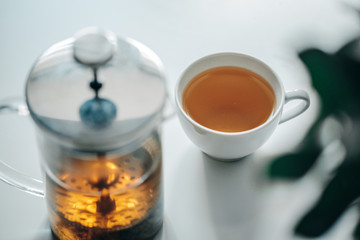 Cup of tea with pot on the white table, green leafs on right side