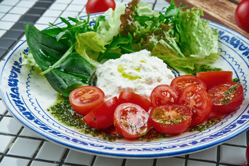 Close up view on appetizing salad with Italian strachatella cheese, lettuce, cherry tomatoes in beautiful blue ceramic plate on white background. Tasty food. Flat lay
