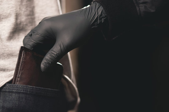 wallet money. Close up of a the hand of thief Pickpocket stealing a purse from the back jeans pocket of a man walking outdoors on a road night dark background.  Crime in an economic downturn concept.