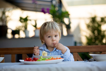 Cute child, toddler blond boy, eating spaghetti in garden