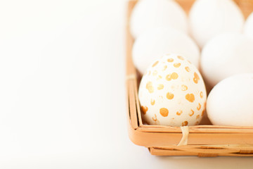 One handpainted egg with gold dots in wicker plate with fresh eggs. One stand out from crowd. Happy Easter background. DIY. Copy space.