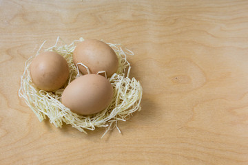 Decorative Easter background for a postcard. Three farm hens unpainted fresh eggs in a decorative sisal nest against a light plywood background with a copy space