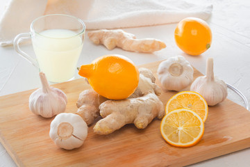 Ginger, garlic, lemon, dried medical chamomile in a jar and ginger tea - a means to protect against viral infections and colds on a light wooden table.