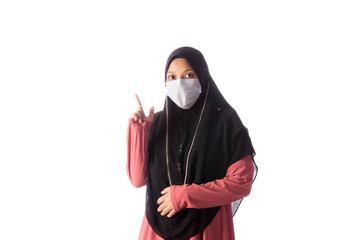 Beautiful southeast asian muslim female in hijab wearing face mask doing a hand gesture isolated over white background.