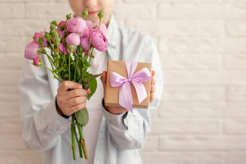 Cute boy holding gift box and bouquet flowers for mother a with falling petals. Mother's Day concept