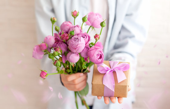 Cute boy holding gift box and bouquet flowers for mother a with falling petals. Mother's Day concept