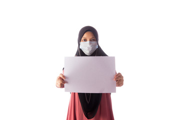 Beautiful southeast asian muslim female in hijab wearing face mask holding a blank paper isolated over white background.