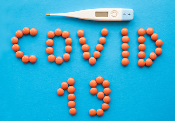 Top view of word COVID - 19 and thermometer on blue background.