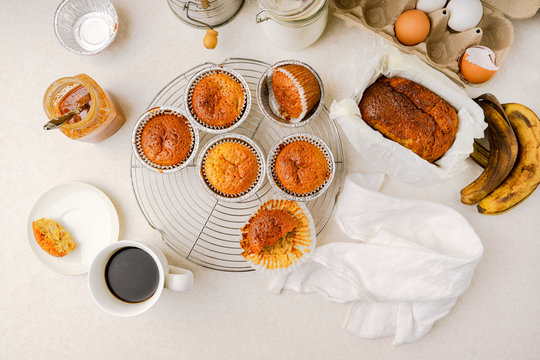 Homemade banana and honey muffins, banana bread, cup of coffee, and various ingredients, top view, horizontal image