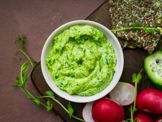 Green pea hummus, fresh greens, vegetables, ckackers served on a wooden board, closeup view