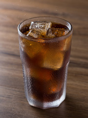 Copo de refrigerante de cola gelado com cubos de gelo sobre mesa de madeira
