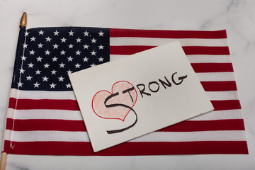 Red heart with the word strong painted in black on white canvas with an American flag laying in the background 