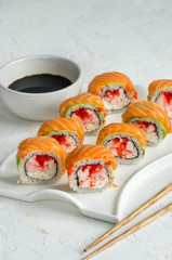 Salmon sushi set on a white plate. Sushi roll with red fish, salmon, red caviar. Roll with fresh salmon, soft avocado, with shrimp and crab and cream cheese under a wide layer of massago caviar.
