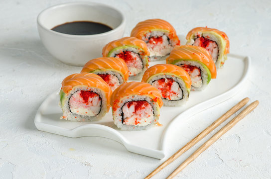 Salmon sushi set on a white plate. Sushi roll with red fish, salmon, red caviar. Roll with fresh salmon, soft avocado, with shrimp and crab and cream cheese under a wide layer of massago caviar.