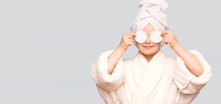 Banner view of beautiful kid girl with towel on head hold cotton pad disk cleansing face skin with cleanser. Happy girl remove makeup enjoy healthy clean skincare beauty treatment concept