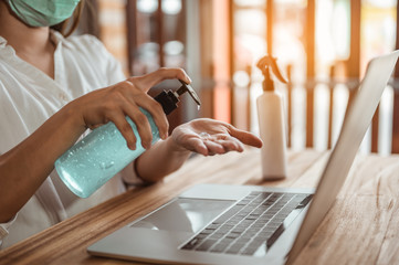 Office worker working from home during coronavirus outbreak cleaning her hands with sanitizer gel and wearing protective mask. Coronavirus, covid-19, Work from home (WFH), Social distancing concept.