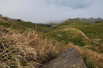 Misty foggy mountain landscape with rocks in front of the grass.