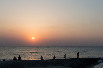 夕日の海岸とシルエットの突堤にいる人々