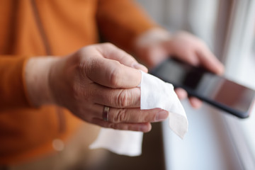Obraz na płótnie Canvas Mature man wipes with a disinfecting cloth heis smartphone after returning home. Safety during COVID-19 outbreak in public places. Epidemic of virus covid.