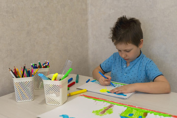 A young Caucasian boy draws with pencils on white paper