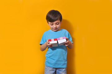 Beautiful cute kid boy looks on two gift present boxes in his hands on the yellow background isolated Holidays surprises