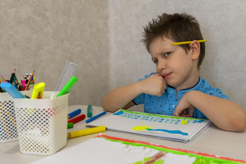 A young Caucasian boy thinks that he can draw with pencils on white paper