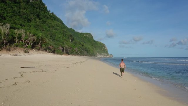 Aerial view athlete runs alone on sandy beach, ocean and mountains on background