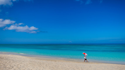 Fototapeta na wymiar Man with a Umbrella walking on the deserted Seven Mile Beach in the Caribbean during confinement, Grand Cayman, Cayman Islands