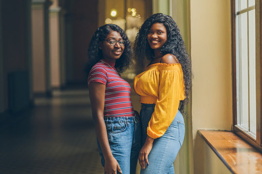 Portrait of two female nigerian students meets in dark university interior. African woman in bright cilor clothes