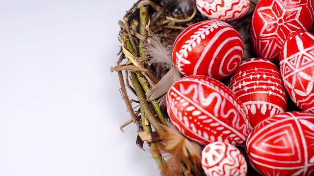 Easter red eggs with folk pattern into bird nest on white background. Hand add eggs to nest. Ukrainian traditional eggs pisanka and krashanka.