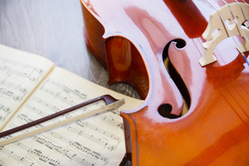 Cello and its bow with a music sheets on wooden background with copy space . Rehearsal before the concert. Musical tuition concept.