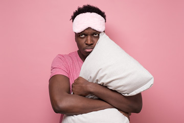 Sad african american man with mask and pillow being stressed staying alone