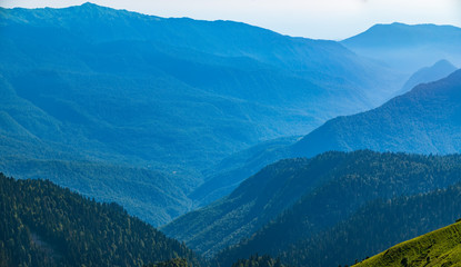 View over the Green Valley, surrounded by high mountains on a summer sunset. Layers of mountains in the haze during sunset.