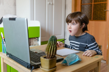 Distance learning for children during the coronavirus epidemic. A boy sits at a table and performs...