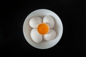 Aerial view of: a white plate, inside, four white eggs, on top of them an egg yolk, the whole set on a black background