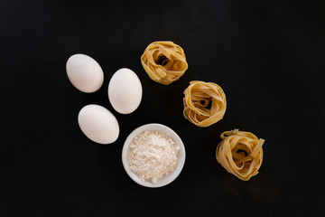 Fototapeta na wymiar White eggs, a ceramic bowl with flour and nests of egg pasta, all on a black background.