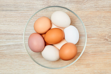 eggs of different colors from white to brown in a glass bowl on a wooden table surface