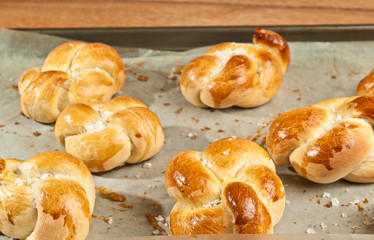 Top view, close distance of, six, freshly baked, homemade, organic, knotted rolls, cooling on parchment paper on a baking sheet, on wood serving board